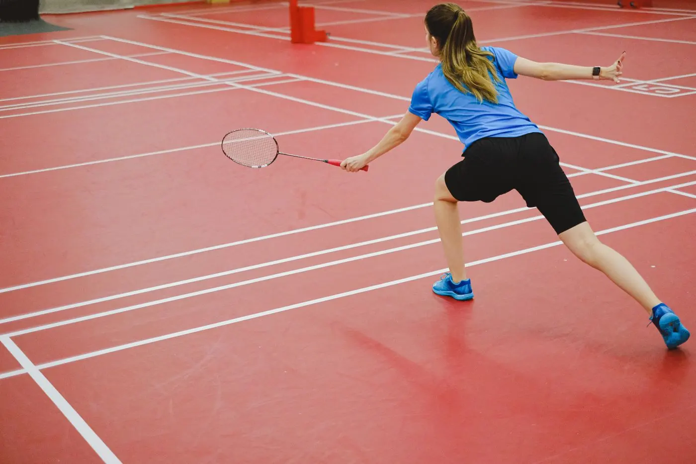 Spielerin auf einem roten Badmintonfeld beim Return